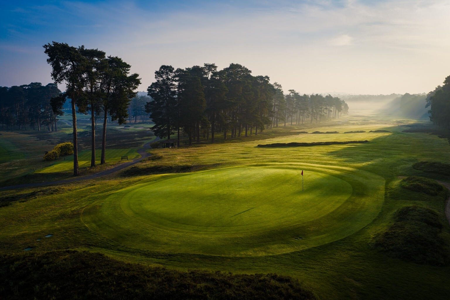 A misty woodland golf landscape photographed from the air in early light