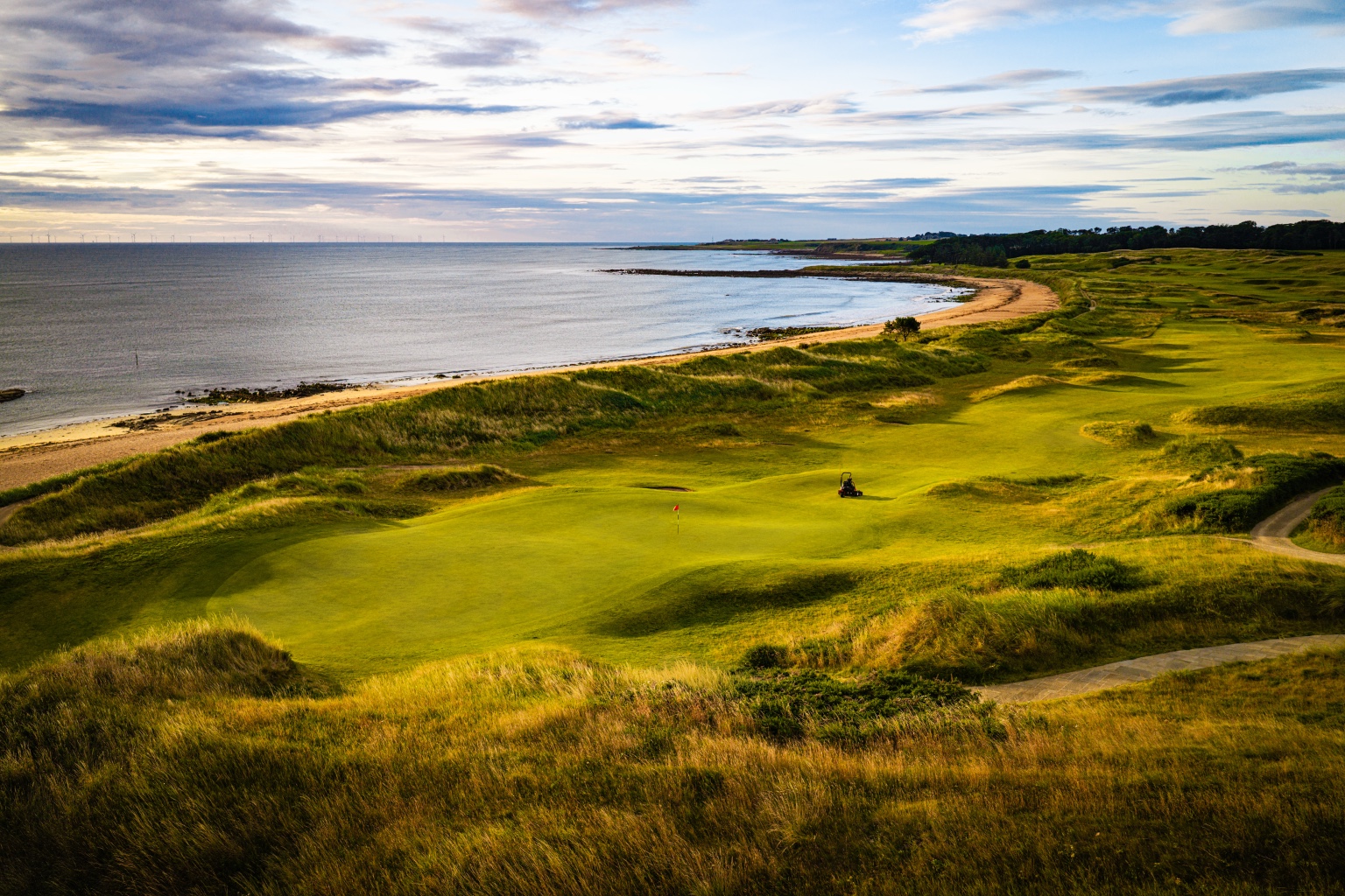 A coastal golf landscape beside a beach beneath a layered sky